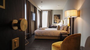 A hotel room with a bed, a chair, a desk with a lamp, and a painting on the wall. - U-Visionary Venezia Hotel (Venice)