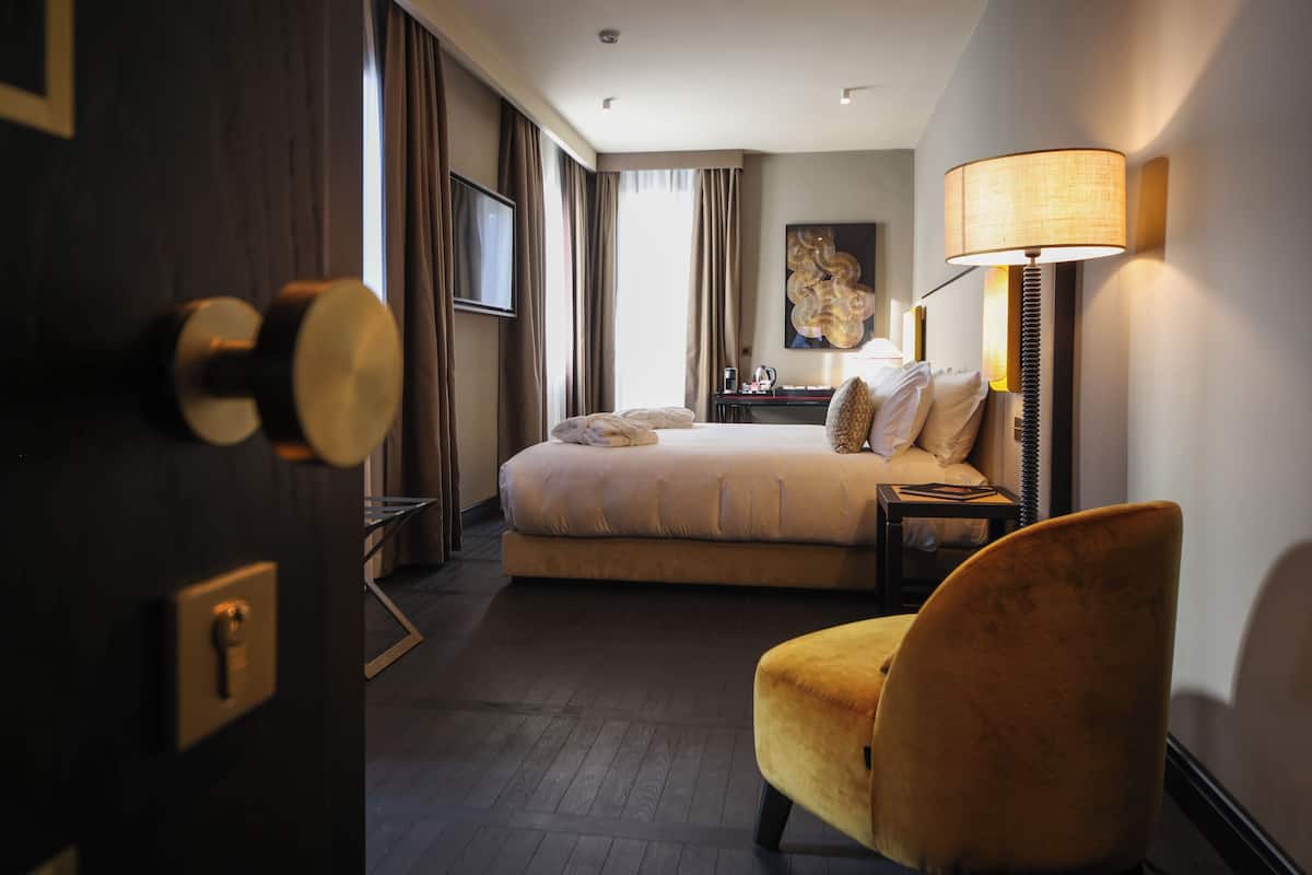 Een hotelkamer met een bed, een stoel, een bureau met een lamp en een schilderij aan de muur.