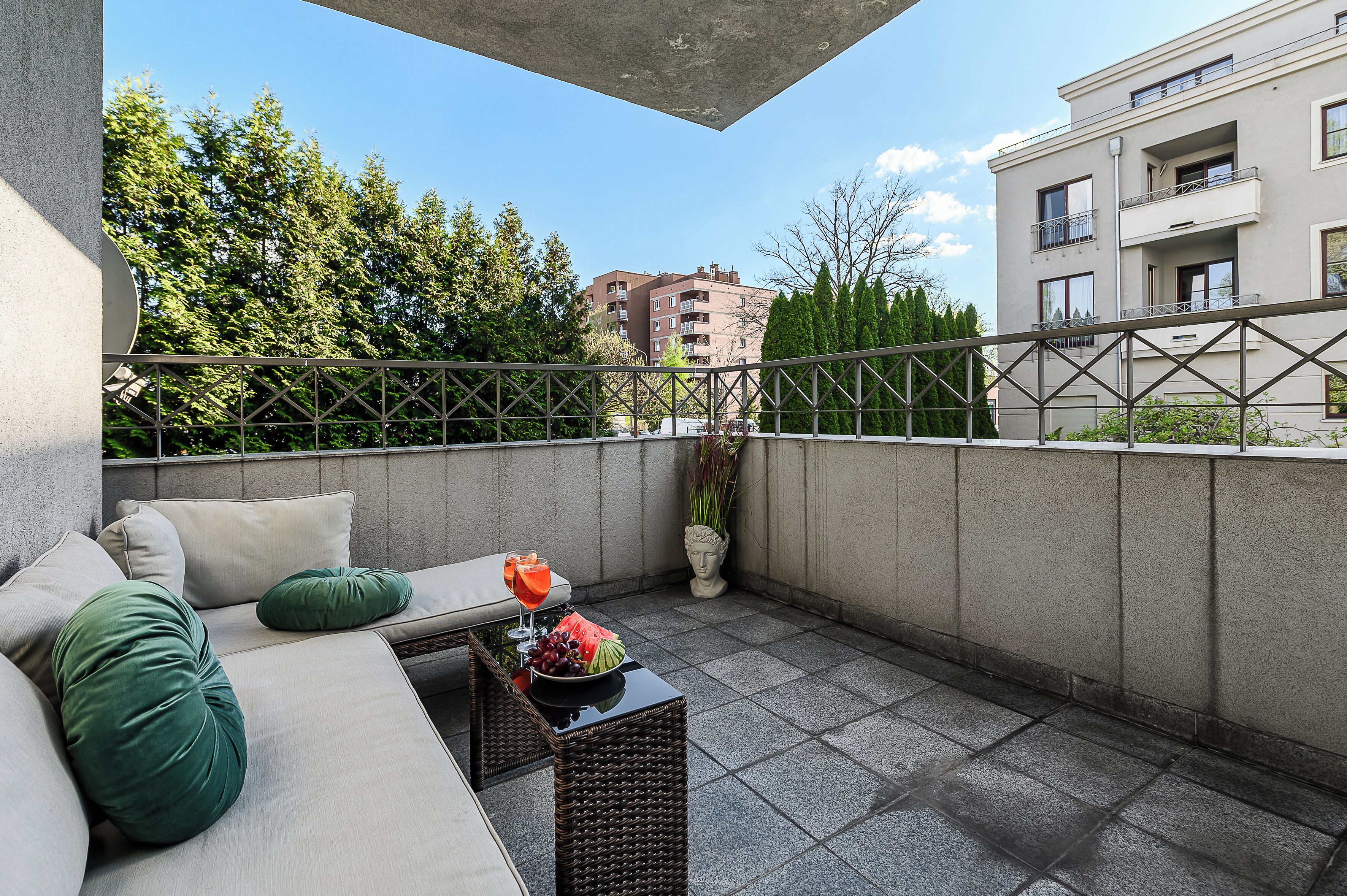 A balcony with a sofa, a small table with a fruit bowl and drink, and a potted plant.