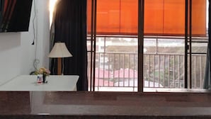 Ein Zimmer mit Deckenventilator, einem Fenster mit orangefarbenen Jalousien, einem an der Wand befestigten Fernseher und einem Waschbecken mit Wasserhahn.