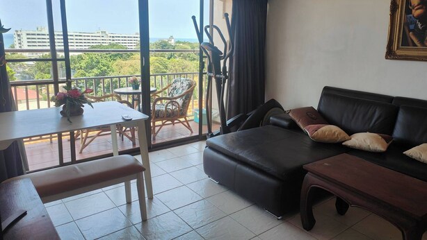 Ein Wohnzimmer mit einer Couch, einem Esstisch mit Stühlen und einem Balkon mit Blick auf Gebäude und Grünflächen.