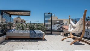 Une terrasse sur le toit avec un jacuzzi, un hamac et un lit recouvert d’une couverture bleue.