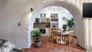 Un intérieur agrémenté d’une arche rustique menant à un espace repas avec des chaises et une table en bois, le tout entouré de plantes en pot et d’un tapis tissé.