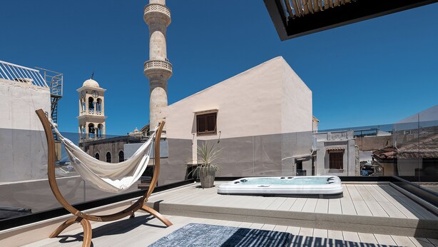 Une terrasse sur le toit avec un hamac, un jacuzzi et une vue sur une mosquée dotée d’un minaret.