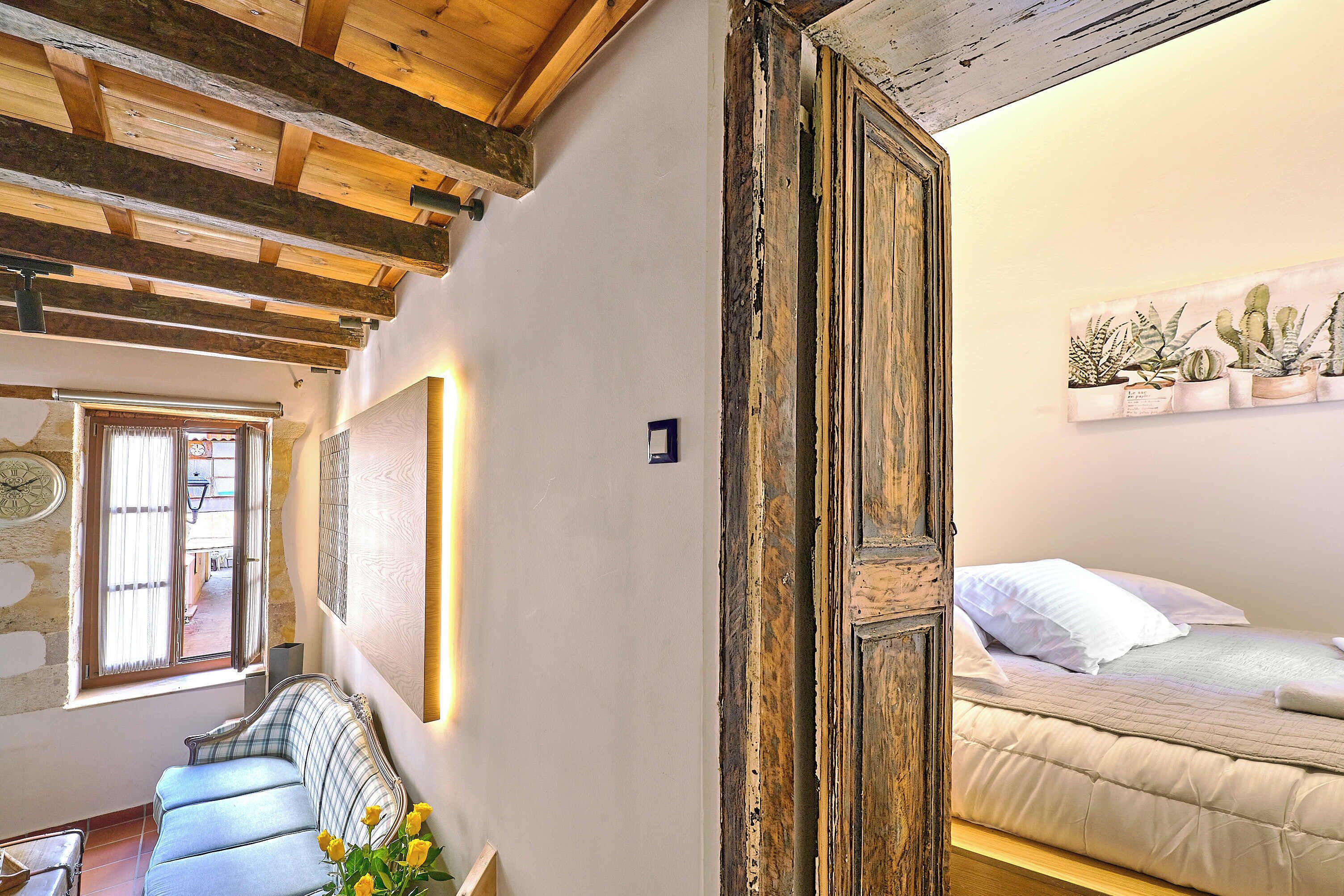 A room with exposed wooden beams, a bed with white bedding, a sofa, and a wall-mounted cactus plant.