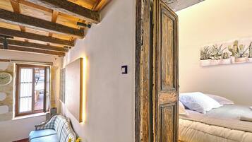 A room with exposed wooden beams, a bed with white bedding, a sofa, and a wall-mounted cactus plant.