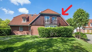 Ein zweigeschossiges Haus mit rotem Ziegeldach, einem Balkon und einem gepflegten Rasen.