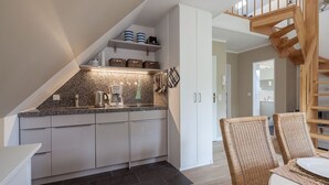 Eine moderne Küche mit Granit Arbeitsplatten, weißen Schränken und einem eingebauten Herd. Es gibt eine Essecke mit Korbstühlen und einem Tisch.