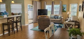A living room with a sofa, TV, and a dining area with chairs and a table.