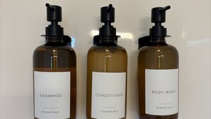 Three bottles of shampoo, conditioner, and body wash with pump dispensers, labeled 'Essentials,' against a plain background.