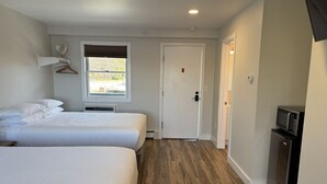 A hotel room with two beds, a window, a door, and a small kitchenette.