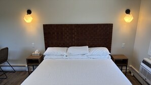 A large bed with a wooden headboard, two bedside tables, a chair, and wall-mounted lights. - Juniper Motel-King Suite-Room 22*Cook Top*Waterfront*Lake Access*Dock (Greenville)