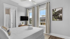 A bedroom with a bed, a flat-screen TV, a window with curtains, and a framed picture on the wall. - Inlet Beach Retreat With Rooftop Views, 4 Bikes + Free Attraction Tickets! (Panama City Beach)