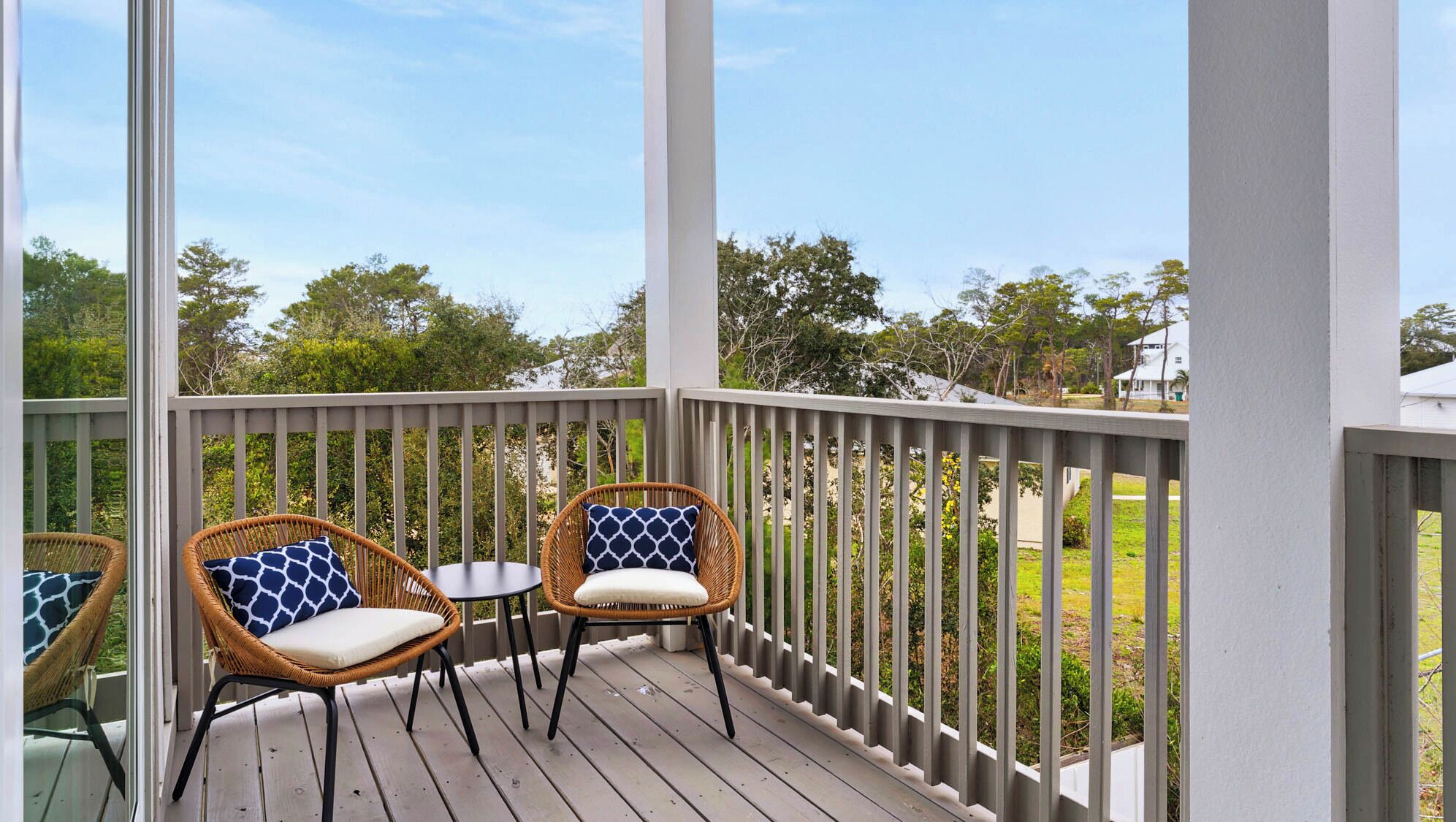 A covered outdoor deck with two wicker chairs and a small table, surrounded by a white railing.