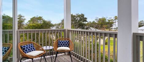 A covered outdoor deck with two wicker chairs and a small table, surrounded by a white railing.