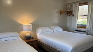 A hotel room with two beds, a bedside table with a lamp, a window with curtains, and a wall-mounted fan. - Juniper Motel*Double Queen*RM 14*Waterfront*Pet Friendly*Dock (Greenville)