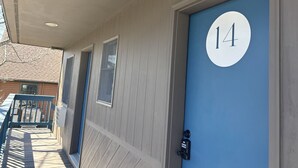 A building exterior with a blue door marked with the number 14, a wooden deck, and a window. - Juniper Motel*Double Queen*RM 14*Waterfront*Pet Friendly*Dock (Greenville)
