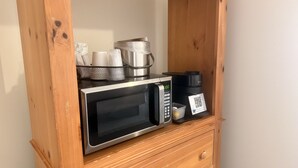 Un four à micro-ondes doté d’un écran numérique, une machine à café et un petit récipient posés sur une étagère en bois.