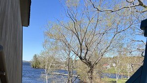 Une vue depuis une véranda donnant sur un lac, avec des arbres et une zone herbeuse.