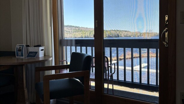 Une pièce avec vue sur un lac, un bureau en bois avec une chaise, et une porte donnant sur l’extérieur.