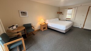 Une petite pièce, bien rangée, avec un lit, une chaise, une table, une lampe et un tableau au mur.
