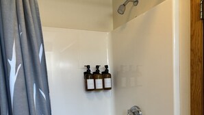 Casa de banho moderna com chuveiro, banheira e sanita. Três garrafas de shampoo e condicionador estão na parede.