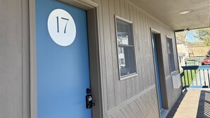 Uma casa com porta azul marcada com o número 17, uma janela pequena e um alpendre com guarda-corpo.