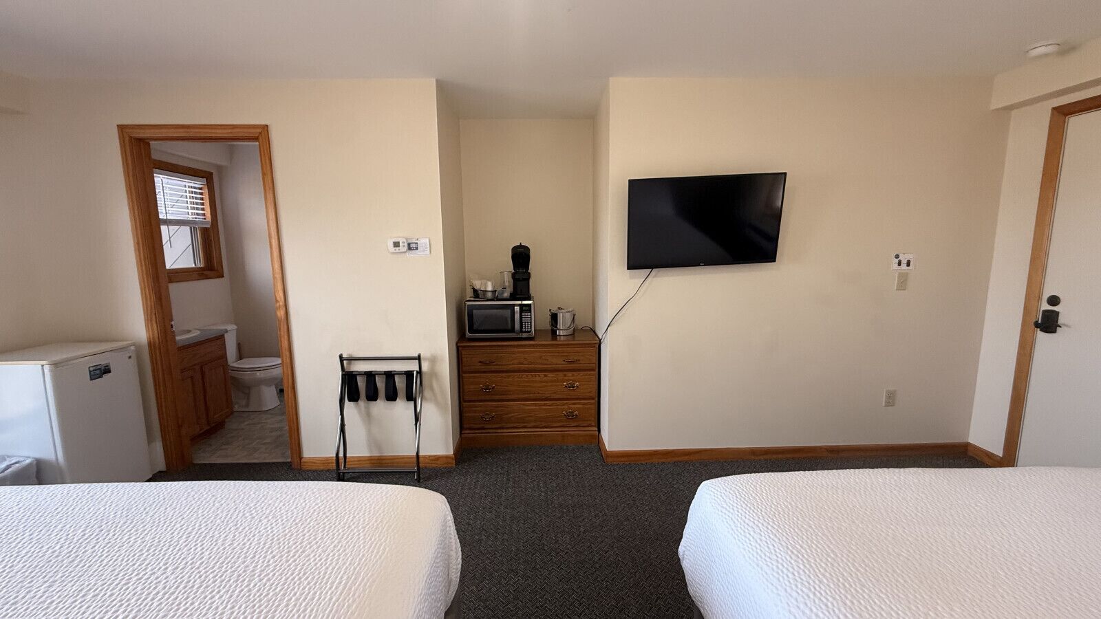 Een hotelkamer met twee bedden, een televisie, een magnetron, een kleine koelkast, een wastafel en een raam met jaloezieën.