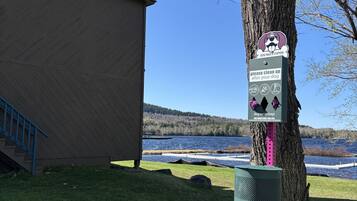 A dog waste station with a sign, a building, and a lake view.