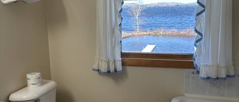 Un baño con inodoro, lavabo y bañera. Hay una ventana con cortinas y vistas al mar.