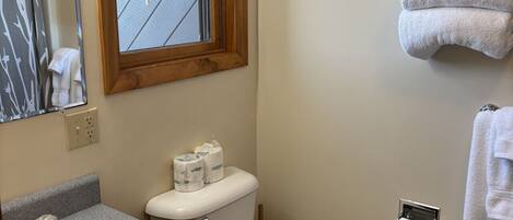 Une salle de bain comprenant des toilettes, un lavabo, un meuble-lavabo, un porte-serviettes et une fenêtre avec des stores.