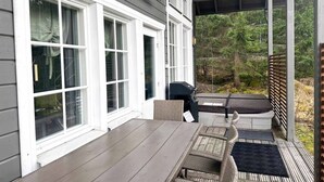Eine überdachte Veranda mit Tisch, Stühlen, einem Grill und Blick auf ein bewaldetes Gebiet.