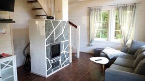 Ein modernes Wohnzimmer mit Kamin aus Stein, einem grauen Sofa, einem kleinen runden Tisch und einer Treppe, die in eine obere Ebene führt.