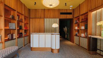 A library with wooden bookshelves, a central reading area with a lamp, and a bench.