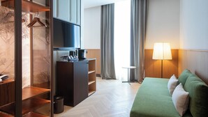 Une chambre d’hôtel avec un canapé vert, une télévision, une petite table avec une lampe et une armoire avec un miroir.