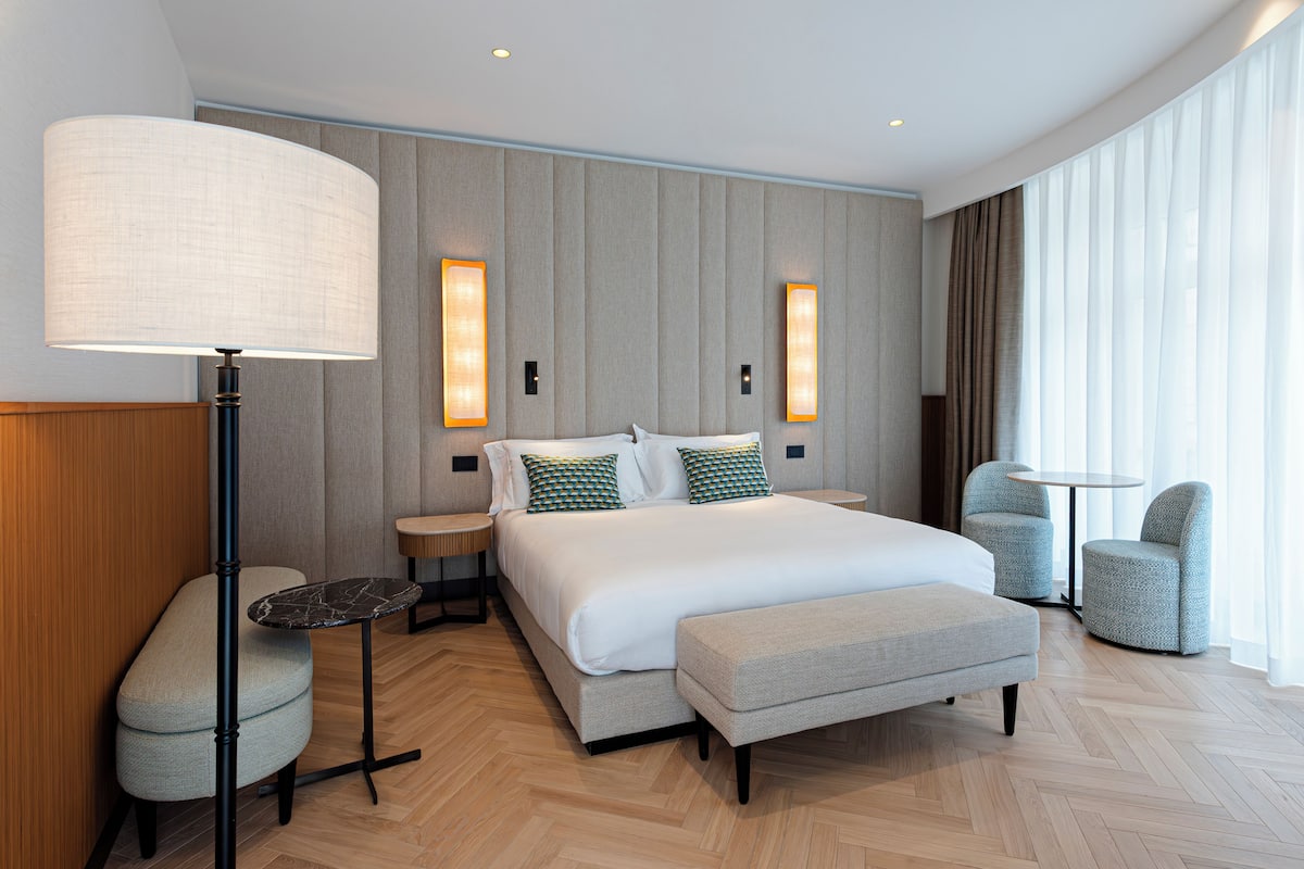 Ein modernes Hotelzimmer mit einem großen Bett, einem Nachttisch, einer Lampe, einem runden Tisch und zwei Stühlen.