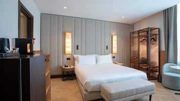 Quarto de hotel moderno com uma cama grande, mesas de cabeceira, guarda-roupa e um espaço de estar.