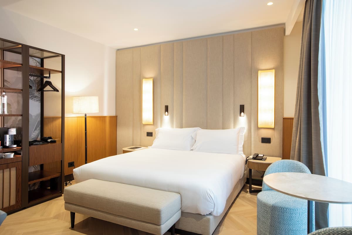 Ein modernes Hotelzimmer mit einem großen Bett, Nachttischen, einem Schreibtisch und einem kleinen runden Tisch.