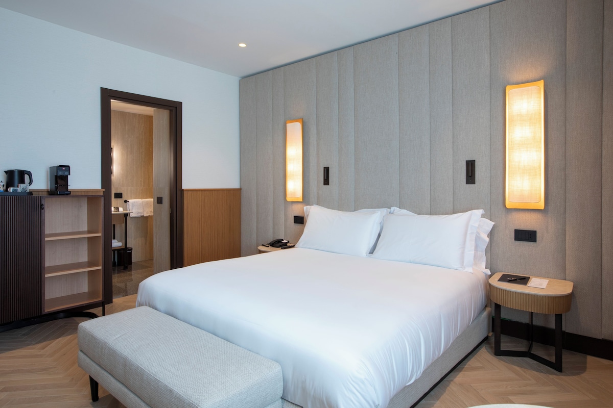 A hotel room with a large bed, bedside tables, a wardrobe, and a coffee machine.