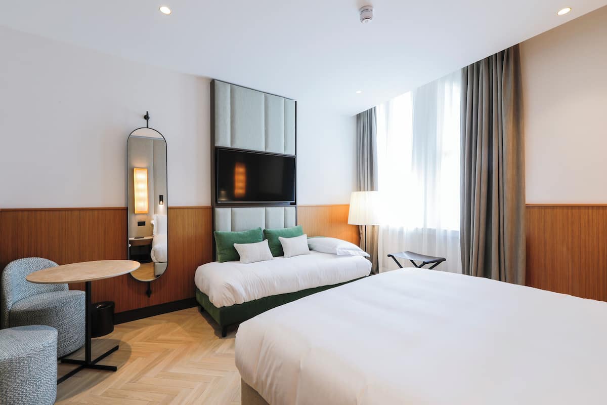 Ein Hotelzimmer mit einem großen Bett, einem Fernseher, einem Spiegel, einem kleinen Tisch und einem Stuhl.