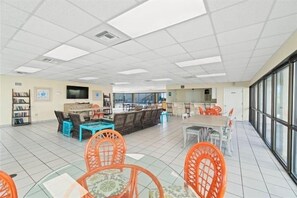 A spacious room with a high ceiling, tiled floor, and a mix of seating arrangements including tables and chairs.