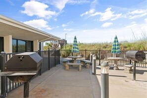 An outdoor patio area with a grill, picnic table, and umbrellas.