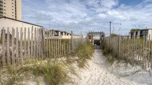 A sandy pathway flanked by wooden fences leading to a building with a flat roof. - 1BR Ground Floor, Pets, Beach & Pool, Sleeps 4 (Panama City Beach)