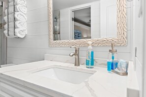 A bathroom with a white sink, a mirror with a mosaic frame, and toiletries on the counter.