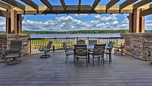 A covered outdoor deck with a table and chairs, overlooking a body of water and greenery.