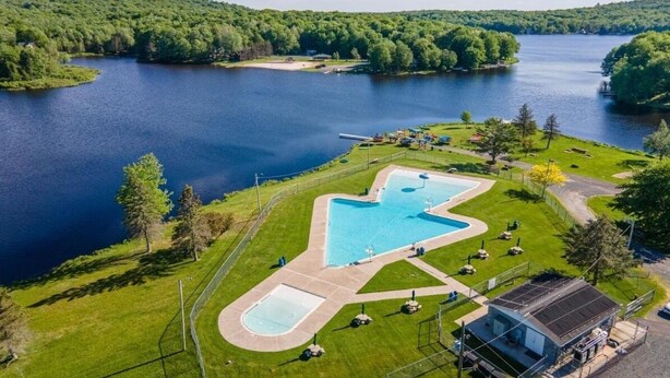 A lakeside property with a swimming pool, a small building, and a fenced area.