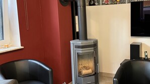 Ein modernes Wohnzimmer mit Kaminofen, zwei Ledersessel, einem Fernseher und einem Fenster mit dekorativen Glasfeldern.