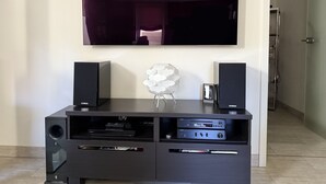 Ein modernes Wohnzimmer mit einem an der Wand befestigten Flachbildfernseher, einer schwarzen Unterhaltungsanlage mit Lautsprechern und Audioausrüstung sowie einer dekorativen weißen Skulptur.