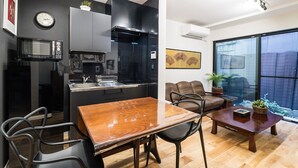 A modern kitchen with a microwave, sink, and cabinets. There is a dining table with chairs and a sofa in the living area. - Gion Dinosaur (Kyoto)
