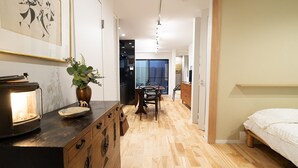 A modern hotel room with a wooden floor, a bed, a dining area with a table and chairs, and a kitchen area with a stove and a plant. - Gion Dinosaur (Kyoto)